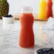 A clear polycarbonate salad dressing / juice bottle filled with orange juice next to a pineapple.