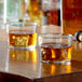 Two Arcoroc old fashioned glasses with ice and amber liquid on a table.