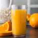 A Carlisle clear plastic tumbler filled with orange juice with a slice of orange on the rim.