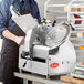 A man in a blue shirt and apron using an Avantco meat slicer on a counter.