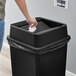 A person throwing a white tissue into a Lavex black square trash can.
