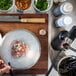 A person using a Breville Smoking Gun to smoke food in a bowl on a cutting board.