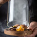 A person using a Breville smoking gun to add smoke to food in a glass jar.