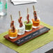 An Acopa flight tray with small glass carafes filled with sauces on a table.