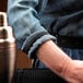 A person wearing a black shirt with a Barfly black shirt sleeve armband holding a drink on a counter.