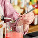 A person using a Barfly stainless steel measuring spoon to pour liquid into a glass.