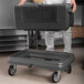 A man using a Metro Mightylite black top loading food pan carrier to transport food.