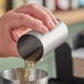 A person using a Barfly stainless steel thimble measure to pour liquid into a glass.