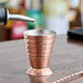 A copper-plated stainless steel measuring jigger on a table.