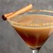 A glass of brown liquid with a DaVinci Gourmet Pumpkin Pie cocktail garnished with a cinnamon stick.