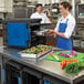 A woman in a blue apron using a Metro Mightylite black food pan carrier with a blue door.