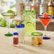 A group of Acopa glass pitchers with green rim filled with different colored drinks.