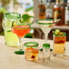 An Acopa Tropic glass pitcher with a green rim on a table with a variety of different colored drinks.