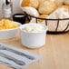 A Tuxton bright white china bouillon cup filled with coleslaw next to a bowl of food and a basket of bread.