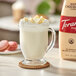 A glass mug of Torani white chocolate drink with whipped cream on top on a white coaster.