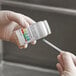 A hand holding a white bottle with green and red labels.