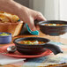 A person holding a pair of HS Inc. charcoal polypropylene serving bowls filled with soup.