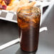 A Cambro amber plastic tumbler filled with brown liquid and ice on a table.