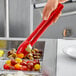 A person holding a Carlisle red plastic utility tong to a bowl of olives.