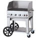 A Crown Verity stainless steel mobile outdoor grill on a cart with a lid.