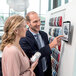 A man and woman using a Durable silver metal wall-mount tablet holder.