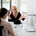 A woman showing a tablet on a wall-mounted tablet holder to another woman.