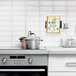 A silver metal wall-mount tablet holder in a home kitchen above a counter with a stove and oven.