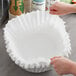 A hand holding a white paper coffee filter.