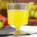 A close-up of a Fineline clear plastic wine cup filled with yellow liquid and a strawberry on the rim.