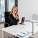 A woman sitting at a desk using a Durable silver metal table clamp tablet holder with a swinging arm.