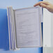 A hand using a Durable Sherpa wall-mount reference system to view a document in a white folder.