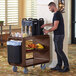 A man standing next to a Cambro dark brown service cart with food on it.