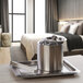 A silver stainless steel ice bucket with ice in it and tongs on a tray.