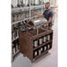 A man standing next to a dark brown Cambro beverage and service cart filled with silverware.