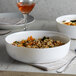 A close-up of two Arcoroc white opal glass bowls filled with food on a table.