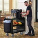 A man standing next to a Cambro black service cart with food on it.