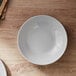 An Arcoroc granite gray opal glass deep coupe plate on a wood surface.