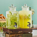 Two Libbey glass beverage dispensers filled with lemonade and cucumber water on a wood surface.