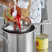 A man using a Choice Coarse China Cap strainer to pour red sauce into a pot.