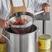 A person in an apron using a Choice Coarse China Cap Strainer to pour red sauce into a pot.