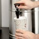 A hand pouring a drink from a Bloomfield 5 gallon iced tea dispenser into a cup.