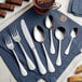 A silverware set with a spoon, fork, and Acopa Vernon stainless steel dinner knife on a napkin next to a glass of tea.