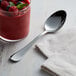 An Acopa Vernon stainless steel oval bowl spoon next to a glass of fruit dessert.