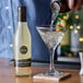 A person pouring Belosa Spicy Dirty Martini Juice into a martini glass.