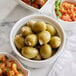 A bowl of Belosa garlic stuffed green olives next to other food on a marble table.