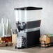 A black and white Crown Beverages plastic beverage dispenser on a table with a glass of ice and a drink inside.