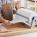 A person in an apron cutting Choice Premium Freezer Paper on a cutting board.