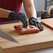 A person wearing black gloves is cutting 10" x 30" PeachTREAT steak paper on a table.