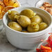 A bowl of green olives and other food on a table.