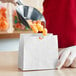 A metal scoop pouring orange candies into a white American Metalcraft mini snack bag.